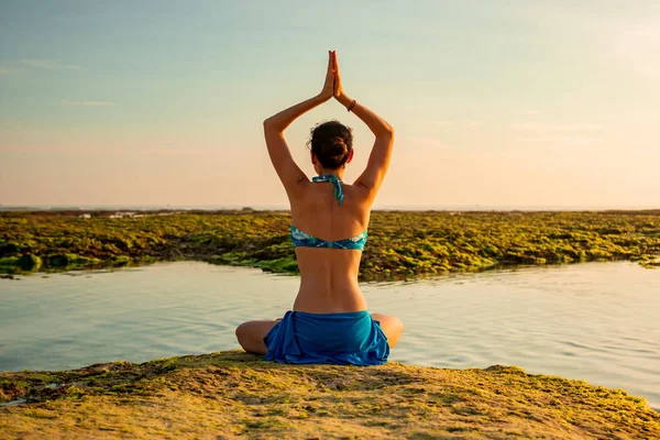 Genç bir kadın, meditasyon yapıyor, yoga yapıyor ve plajda pranayama yapıyor. Günbatımı yoga antrenmanı. Namaste Mudra 'da eller havaya. Arkadan bak. Melasti plajı, Bali — Stok fotoğraf