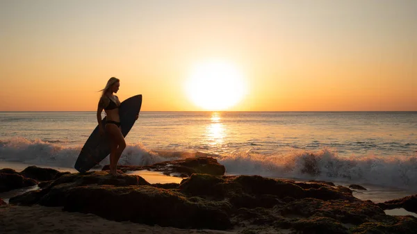 Surf-Lifestyle. Surfermädchen mit Surfbrett am Strand. Silhouette eines Surfermädchens bei Sonnenuntergang. goldener Sonnenuntergang. bali, indonesien — Stockfoto