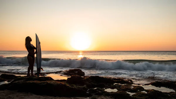 Silhouette di surfista ragazza con tavola da surf sulla spiaggia. Ora del tramonto dorato. Bali, Indonesia — Foto Stock