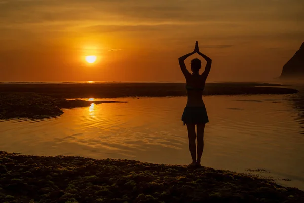 Yoga pozu. Sahilde durmuş, yoga yapan bir kadın. Gün batımının altın saatinde namaste Mudra ile kollarını kaldıran genç kadın. Arkadan bak. Melasti plajı, Bali. 