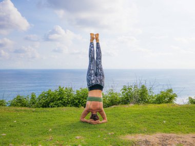 Desteklenen amuda duran beyaz kadın. Salamba Sirsasana. Uçurumun kenarında yoga antrenmanı. Enerjiyi arttır. Endonezya, Bali 'de yoga inzivası