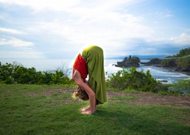 Yoga yapan, Uttanasana pozunda duran genç bir kadın. Öne eğil. Sırtımı esnetiyorum. Uçurumda açık hava yogası. Omurga sağlam. Yoga inzivası. Tanah Lot Tapınağı Bali, Endonezya