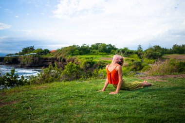 Açık havada yoga pratiği. Bhujangasana 'da Kobra pozu veren genç bir kadın. Hatha yogasında Asana 'ya yaslanarak yaslanıyorlar. Omurga sağlam. Yoga inzivası. Tanah Lot Tapınağı Bali, Endonezya