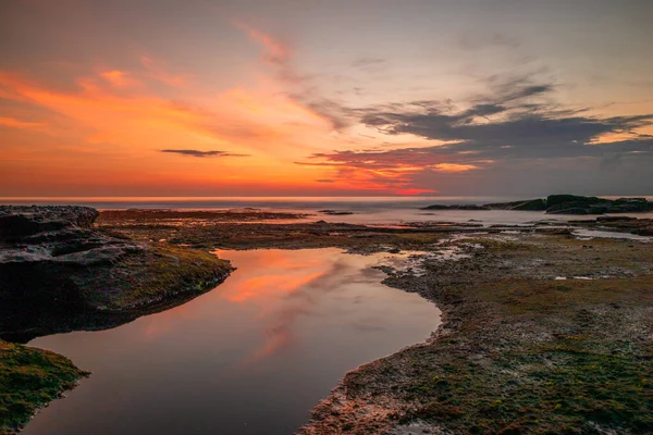 Seascape. Beach with rocks and stones. Low tide. Sun and clouds reflection in water. Slow shutter speed. Soft focus. Tanah Lot beach, Bali, Indonesia — Stockfoto