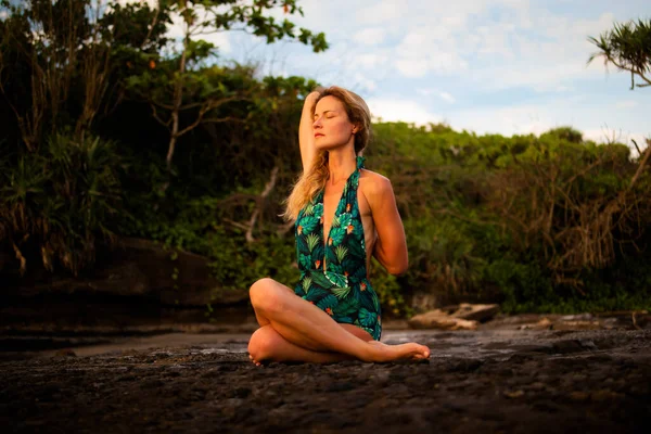 Açık havada yoga pratiği. Gomukhasana, İnek Yüzlü Poz, Hatha yogasında oturan genç bir kadın. Arkasından el ele tutuşan ve esneyen bir kadın. Kişisel bakım konsepti. Tanah Lot Plajı, Bali