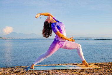 Okyanus manzaralı gündoğumu yoga antrenmanı. Virabhadrasana I, Warrior I Poose 'un varyasyonlarını uygulayan genç bir kadın. Güçlü, sağlıklı bir vücut. Yoga inzivası. Mükemmel vücut şekli. Bali, Endonezya
