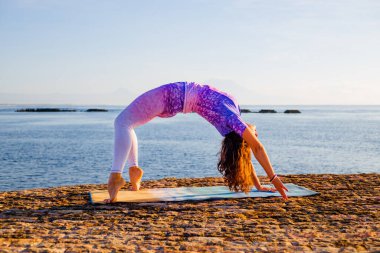 Gün doğumu yogası. Chakrasana ya da Urdhva Dhanurasana, Full Wheel Poose çalışan genç bir kadın. Yukarı bakan yay pozisyonu derin bir arka virajdır. Esneklik, güç ve sabır sağlar. Bali, Endonezya.