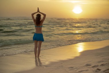 Yoga pozu. Sahilde durmuş yoga yapan bir kadın silueti. Gün batımının altın saatinde namaste Mudra ile kollarını kaldıran genç kadın. Arkadan bak. Güneş ışığı yansıması. Melasti plajı, Bali.