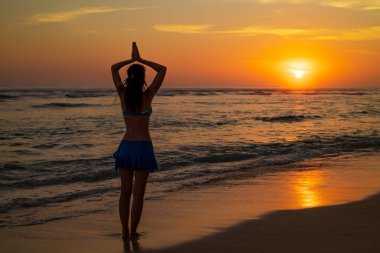Yoga pozu. Sahilde durmuş yoga yapan bir kadın silueti. Gün batımının altın saatinde namaste Mudra ile kollarını kaldıran genç kadın. Arkadan bak. Güneş ışığı yansıması. Melasti plajı, Bali.