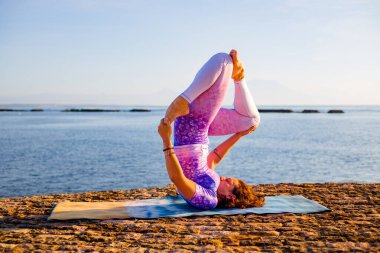 Okyanus manzaralı gündoğumu yoga antrenmanı. Genç bir kadın Niralamba Sarvangasana, Omuz Durağı 'nda pratik yapıyor. Hatha yogasında ters asana. Yoga inzivası. Bali, Endonezya