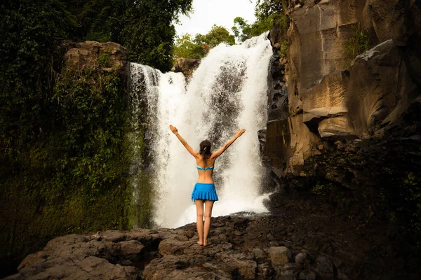 滝で水着を着た若い旅行者の女性 滝の前で腕を上げて興奮した白人女性 後ろから見るんだ テゲヌンガンの滝 旅行のコンセプト ウブド インドネシア — ストック写真
