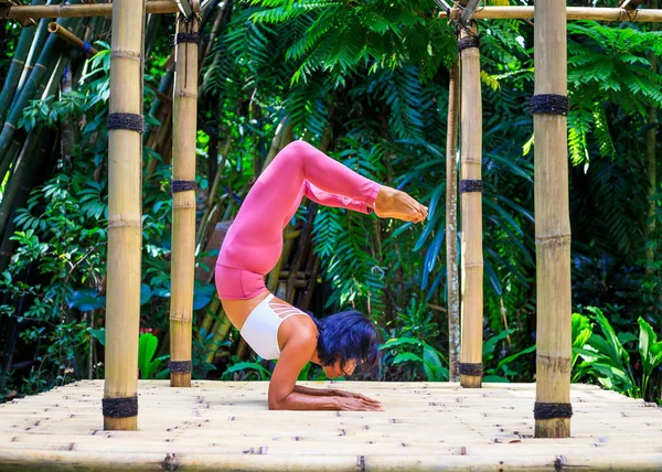 Yoga practice outdoor. Asian yoga teacher practicing Vrischikasana, Scorpion pose. Inverted asana combines a forearm balance and backbend. Support healthy body, improve immune system. Bali, Indonesia