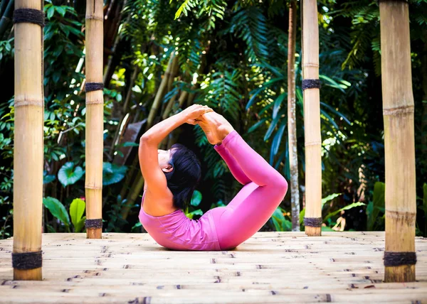 Yoga practice outdoor. Asian yoga teacher practicing Dhanurasana, Bow Pose. Backbending asana in hatha yoga. Flexible spine. Support immune system. Self care concept. Bali, Indonesia