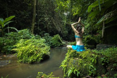 Genç beyaz kadın kayanın üzerinde oturmuş yoga ve pranayama yapıyor. Namaste Mudra ile kol kola. Arkadan bak. Asya 'da tatil. Sakin ve rahatlatıcı bir atmosfer. Yoga inzivası. Bangli, Bali.