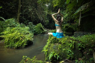 Genç beyaz kadın kayanın üzerinde oturmuş yoga ve pranayama yapıyor. Namaste Mudra ile kol kola. Arkadan bak. Sağlık sigortası konsepti. Sakin ve rahatlatıcı bir atmosfer. Yoga inzivası. Bangli, Bali.