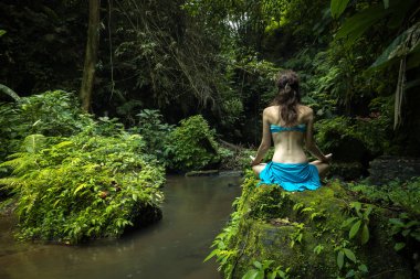 Genç beyaz kadın kayanın üzerinde oturmuş yoga ve pranayama yapıyor. Eller Gyan Mudra 'da. Arkadan bak. Asya 'da tatil. Sakin ve rahatlatıcı bir atmosfer. Tropik doğa manzarası. Bangli, Bali.