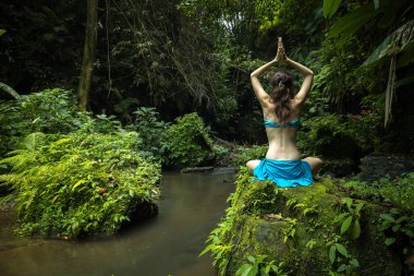 Genç beyaz kadın kayanın üzerinde oturmuş yoga ve pranayama yapıyor. Namaste Mudra ile kol kola. Arkadan bak. Kişisel bakım konsepti. Sakin ve rahatlatıcı bir atmosfer. Yoga inzivası. Bangli, Bali.