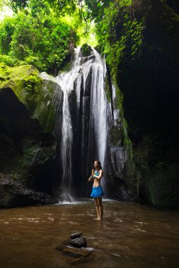 Genç beyaz kadın şelalenin yanında duruyor, meditasyon yapıyor, yoga yapıyor ve pranayama yapıyor. Eller namaste mudra 'da. Konsantrasyon ve rahatlama. Krisik Şelalesi Bangli, Bali, Endonezya 'da.