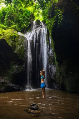 Genç beyaz kadın şelalenin yanında duruyor, meditasyon yapıyor, yoga yapıyor ve pranayama yapıyor. Ellerini namaste Mudra 'ya kaldır. Sağlık sigortası konsepti. Krisik Şelalesi Bangli, Bali, Endonezya 'da.