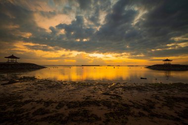 Gün doğumu deniz manzarası. Geleneksel bale çardakları. Bulutlu gökyüzü. Gün ışığı ufukta. Renkli gün doğumu. Dalgalar çekildiğinde kumsal. Nusa Dua, Bali, Endonezya.