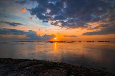 Gün doğumu deniz manzarası. İnanılmaz bir su yansıması. Bulutlu gökyüzü. Gün ışığı ufukta. Renkli gün doğumu. Taşlı ön plan. Sakin su yüzeyi. Nusa Dua Sahili, Bali, Endonezya.