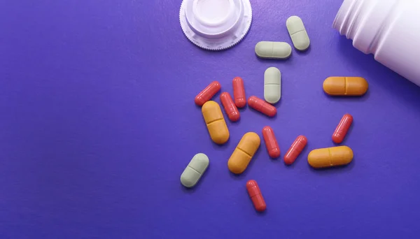 Assorted pharmaceutical medicine pills, tablets and capsules. Pills on purple background. Heap of assorted various medicine tablets and pills different colors on background. Health care