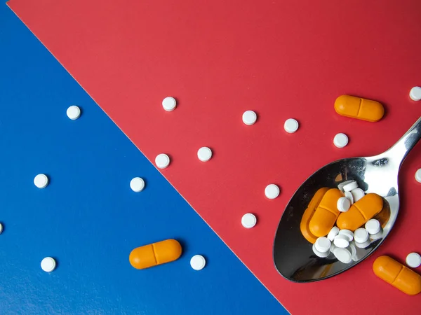 medicine pills, tablets and capsules. Blue and red background. Heap of assorted various medicine tablets and pills on spoon different colors on background. Health care