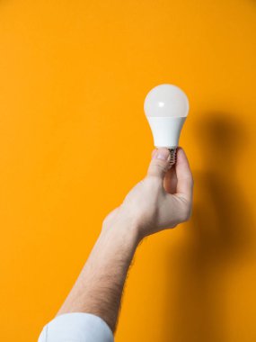 The hand of a man holding a light bulb for innovation and creative concept. Light bulb in hand on a yellow background. Empty space for your text