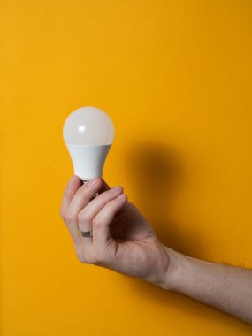 The hand of a man holding a light bulb for innovation and creative concept. Light bulb in hand on a yellow background. Empty space for your text