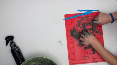 Küçük çocuk faiziyle kilden heykel yapıyor. Çocuklar için çömlek atölyesi, işlenmemiş kil, heykel aletleri, cilalama ve kil boyama. Çocuklar elleri yakın.