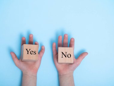 Tahta küplere EVET ve HAYIR kelimeleri. Doğru çözümü seçme kavramı. Çocuğun eli engeli tutuyor, bir seçim yapıyor, oylar mavi arka planda doğru karar için