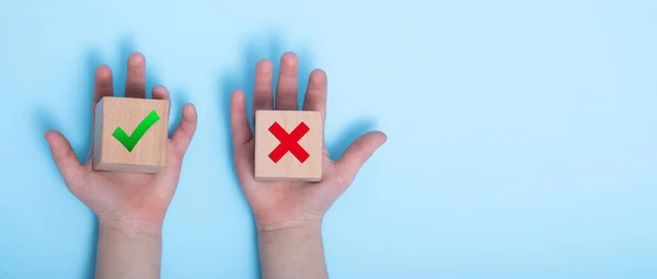 close-up of a hands placing two wooden blocks on a blue background. True and false symbols accept rejected for evaluation, Yes or No on wood blocks on blue background.