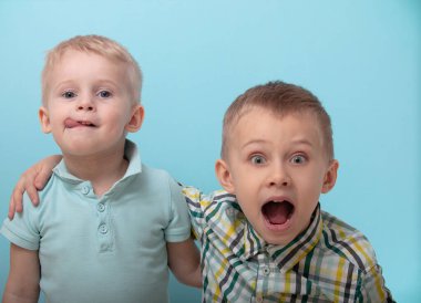 İki erkek birbirine dostça sarılıyor ve şaşırmış yüzler sergiliyorlar. Mavi arka plandaki çocuklar