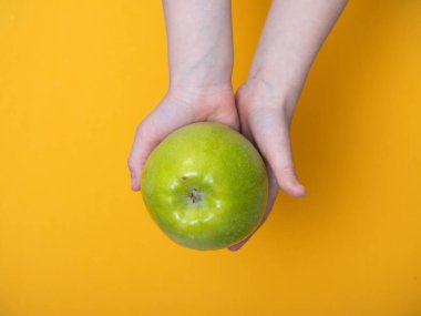 Sarı arka planda bir çocuk elinde yeşil bir elma tutuyor.