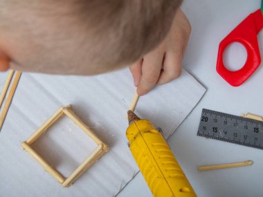 Bambu çubuklarından ev yapmak için adım adım talimatlar. Çocukların yaratıcılığı, el işi, online dersler. Dördüncü adım tutkal tabancasıyla, çocuk bambu çubukları takıyor.