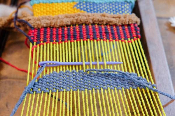 Modern weaving on a loom, Threading purple needle on strands of frame. Craft and handcraft.