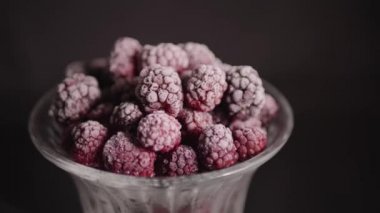 Donmuş ahududu, siyah arka planda bir bardakta, renk gölgeli.