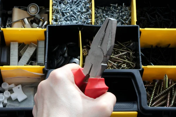 Un conjunto de herramientas en una caja de plástico, alicates en una mano . — Foto de Stock