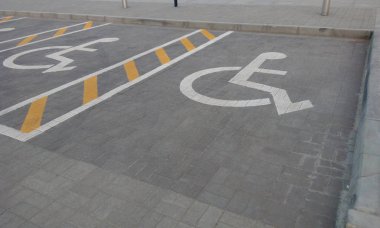 Tekerlekli sandalyedeki kişi için ayrılmış engelli park yeri olan asfalt yol.