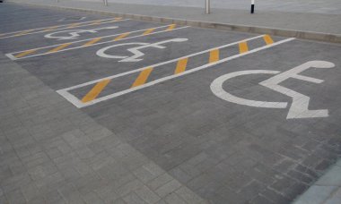 Tekerlekli sandalyedeki kişi için ayrılmış engelli park yeri olan asfalt yol.