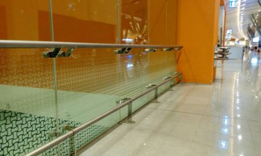 Sertleştirilmiş cam. Tam boy cam bölme. Paslanmaz çelik el demiryolu koruması ve turuncu renkli arka plan duvarları var.