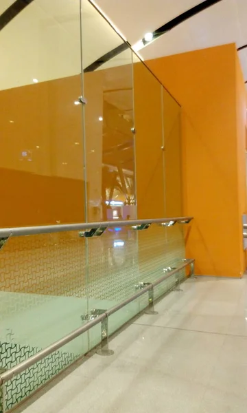 Sertleştirilmiş cam. Tam boy cam bölme. Paslanmaz çelik el demiryolu koruması ve turuncu renkli arka plan duvarları var. — Stok fotoğraf