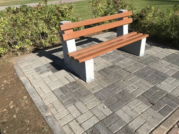 A wooden bench with concrete supports built in between the interlock floor tile flooring isolated for a healthy and relax conversation with friend or family relative in a park or outdoor