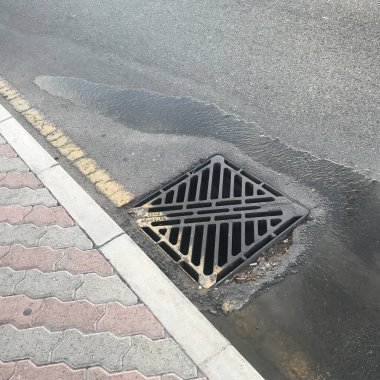 Toprağın dengesiz yerleşimine yol açan sıkıştırmadaki kötü işçilikten dolayı rögar kapağından su çekiliyor.