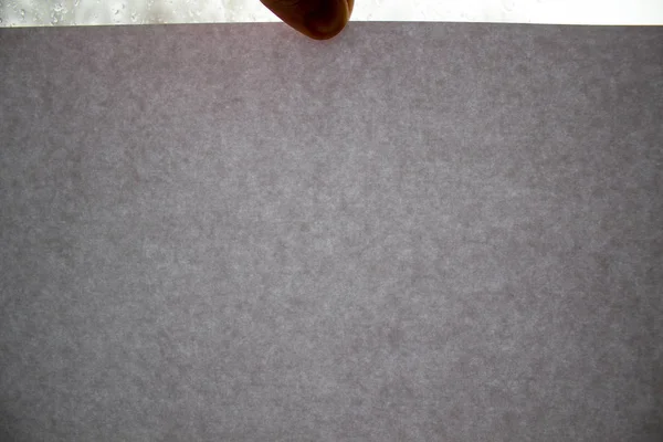 Un uomo tiene una pagina di cartone grigio sullo sfondo di una finestra . — Foto Stock