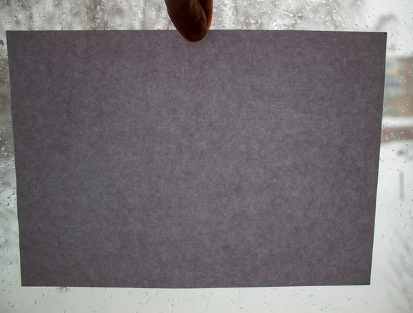 Un uomo tiene una pagina di cartone grigio sullo sfondo di una finestra . — Foto Stock