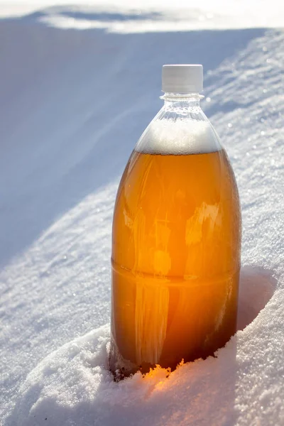 Plastic beer bottle in the snow in winter in nature, beer background.