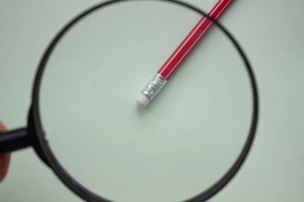 One red pencil under a magnifying glass close-up on a light background.