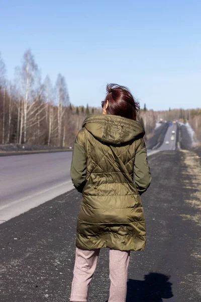 Une jeune femme marche sur le bord de la route. Route dans la forêt — Photo