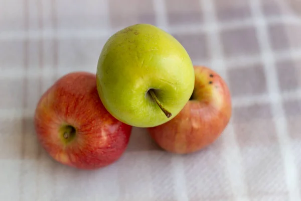 Three apples, one green and two red-yellow on a light background